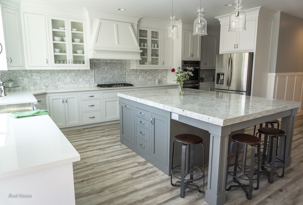 Example of a mid-sized u-shaped medium tone wood floor and brown floor kitchen design with a single-bowl sink, glass-front cabinets, white cabinets, granite countertops, gray backsplash, subway tile backsplash, stainless steel appliances and an island