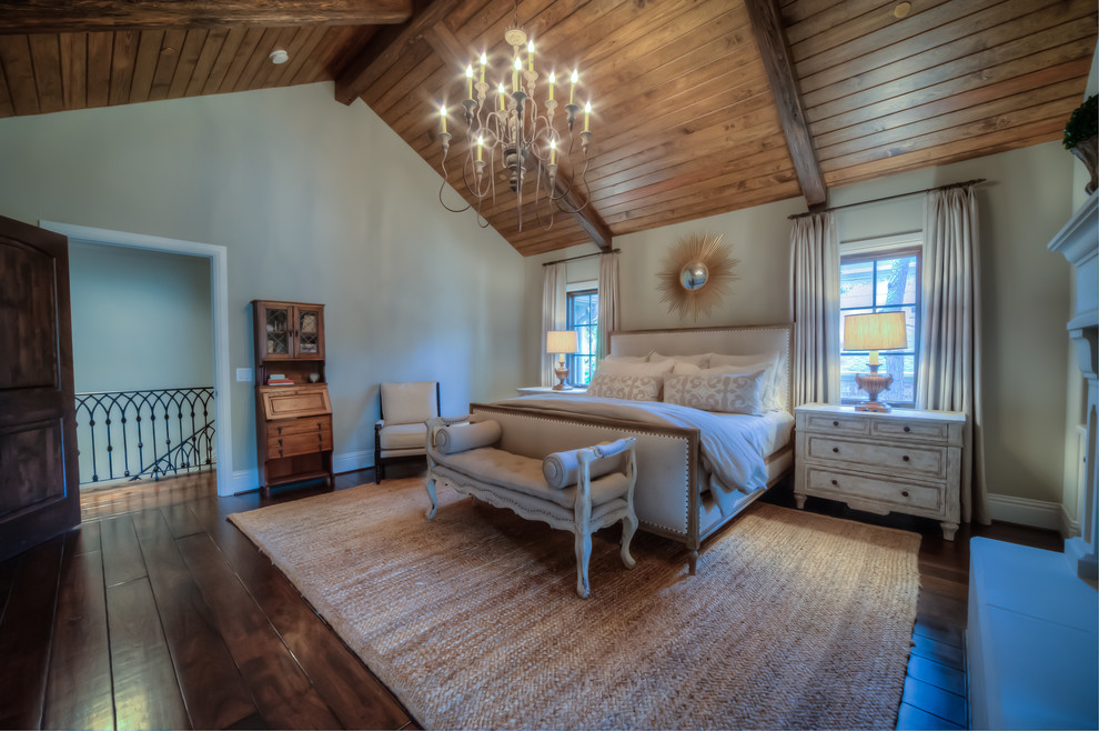 This is an example of a large traditional master bedroom in Houston with white walls, dark hardwood floors, a two-sided fireplace, a wood fireplace surround and brown floor.
