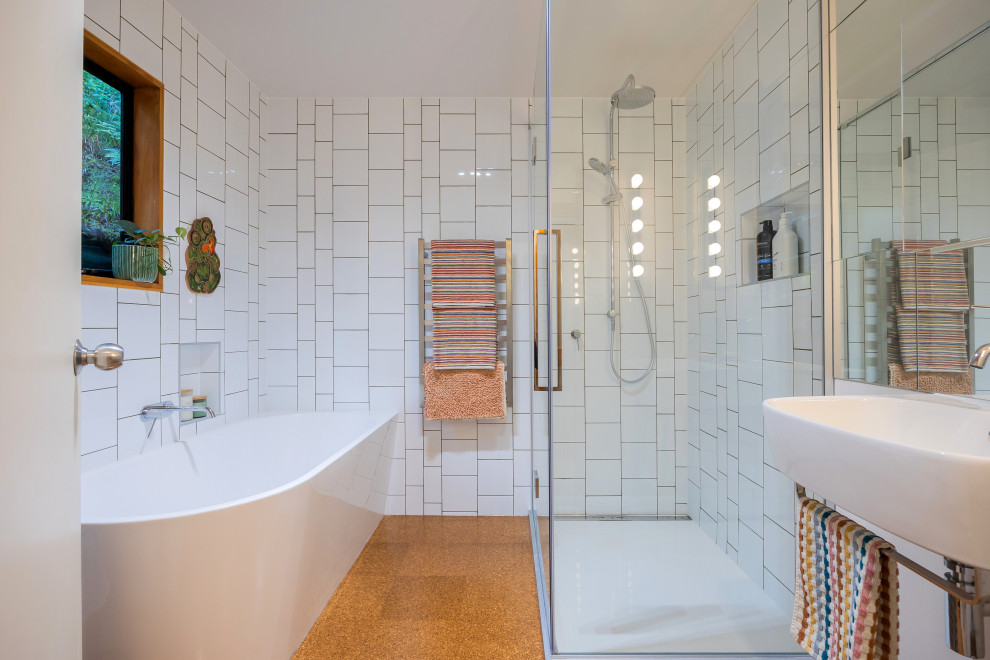 Bild på ett litet eklektiskt badrum, med vita skåp, ett hörnbadkar, en hörndusch, vit kakel, keramikplattor, vita väggar, korkgolv, ett väggmonterat handfat, brunt golv och dusch med gångjärnsdörr