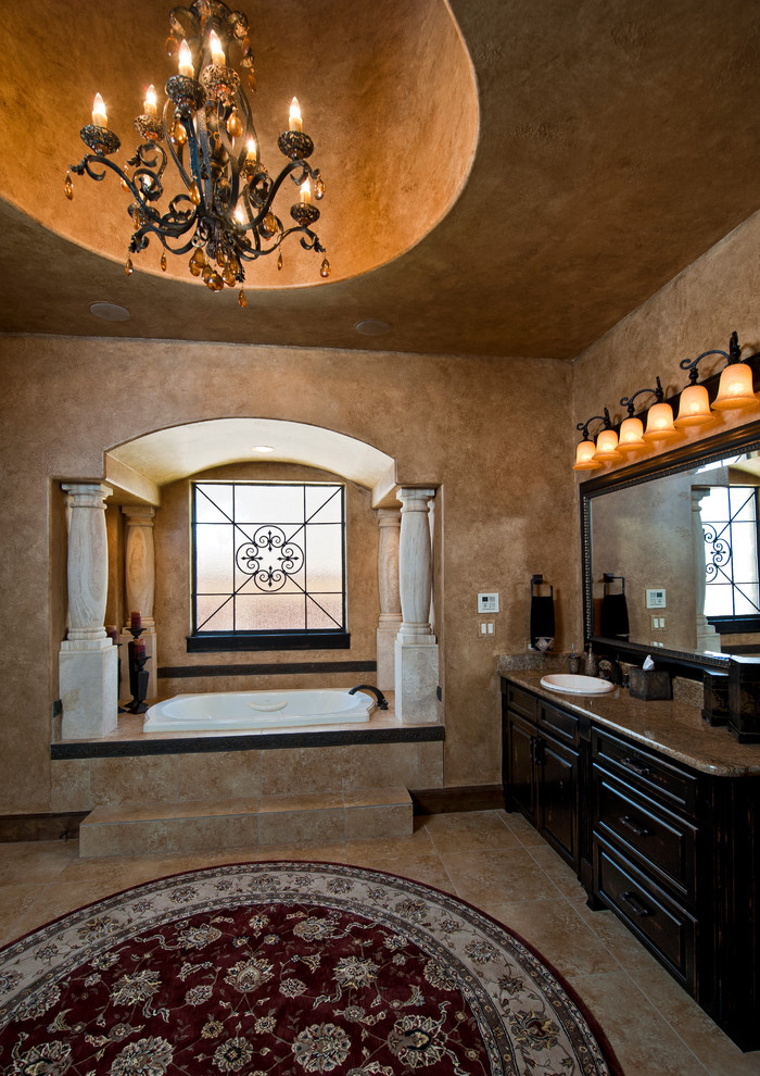 This is an example of an expansive mediterranean master bathroom in Austin with a drop-in sink, dark wood cabinets, granite benchtops, beige tile, beige walls and travertine floors.
