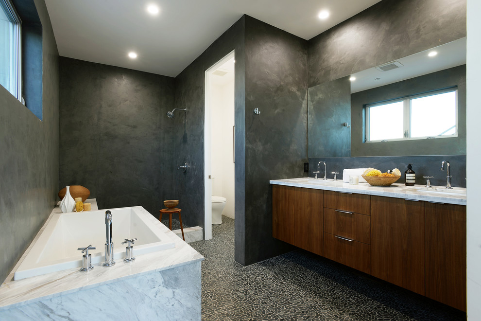 Inspiration for a contemporary bathroom in Other with an undermount sink, flat-panel cabinets, medium wood cabinets, marble benchtops, a drop-in tub, an open shower, a one-piece toilet, gray tile, grey walls, pebble tile floors and an open shower.