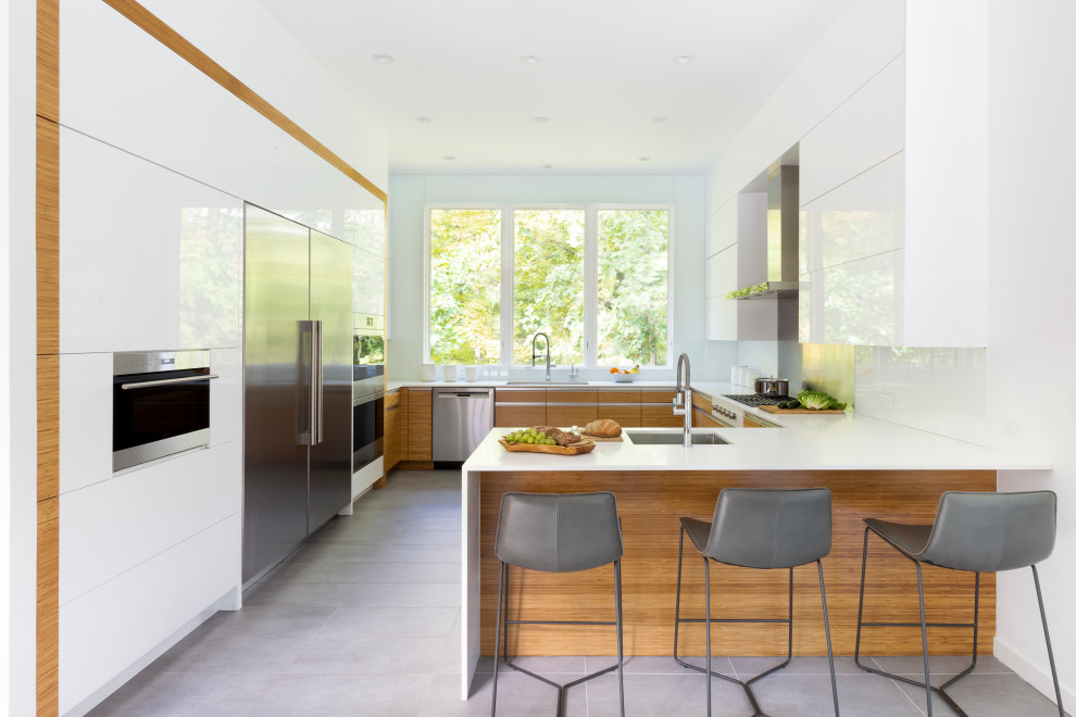 Inspiration for a large contemporary u-shaped kitchen in New York with flat-panel cabinets, white cabinets, engineered stone countertops, white splashback, stone slab splashback, stainless steel appliances, porcelain flooring, a breakfast bar, grey floors, a submerged sink and white worktops.