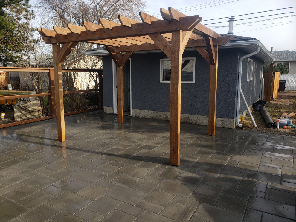 This is an example of a large rustic partial sun backyard concrete paver landscaping in Edmonton with a pergola for summer.