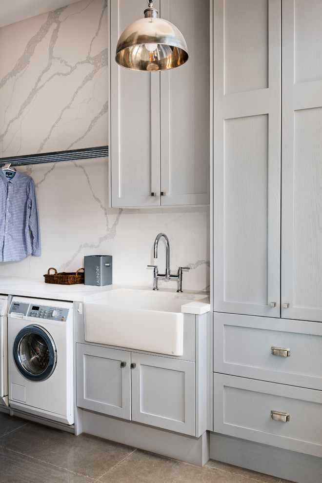 This is an example of an expansive country galley dedicated laundry room in Melbourne with a farmhouse sink, shaker cabinets, grey cabinets, quartz benchtops, concrete floors, grey floor, white benchtop, grey walls and a side-by-side washer and dryer.