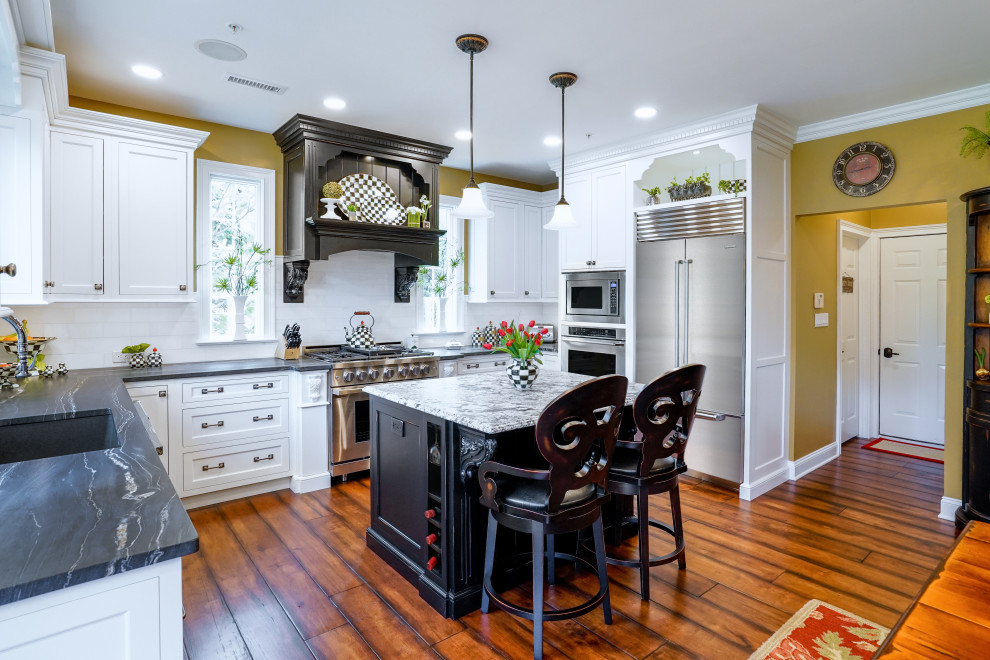 Photo of a large traditional u-shaped eat-in kitchen in Philadelphia with a double-bowl sink, beaded inset cabinets, white cabinets, quartzite benchtops, white splashback, marble splashback, stainless steel appliances, medium hardwood floors, with island, brown floor and black benchtop.