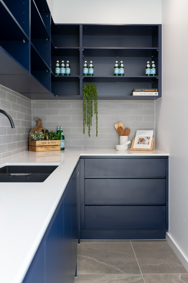 Inspiration for a mid-sized modern l-shaped kitchen pantry in Canberra - Queanbeyan with an undermount sink, blue cabinets, quartz benchtops, grey splashback, subway tile splashback, black appliances, porcelain floors, grey floor and white benchtop.