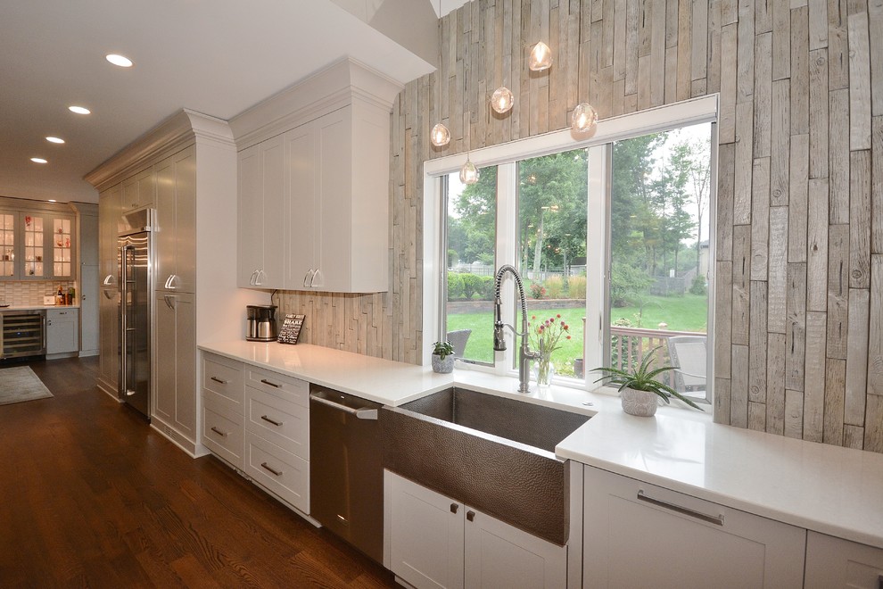 Large transitional u-shaped dark wood floor and brown floor eat-in kitchen photo with a farmhouse sink, recessed-panel cabinets, white cabinets, limestone countertops, beige backsplash, porcelain backsplash, stainless steel appliances, an island and gray countertops
