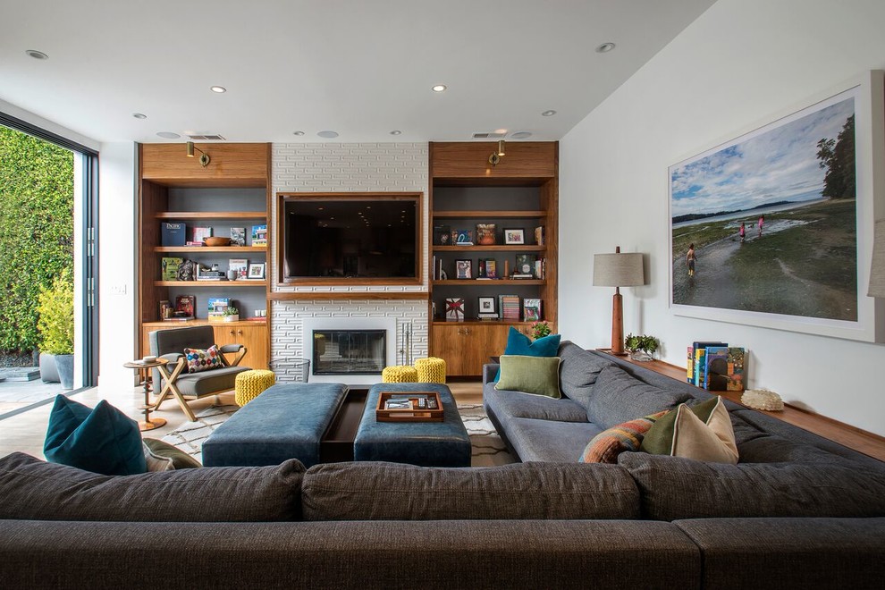 This is an example of a midcentury living room in Los Angeles with white walls, light hardwood floors, a standard fireplace and a wall-mounted tv.