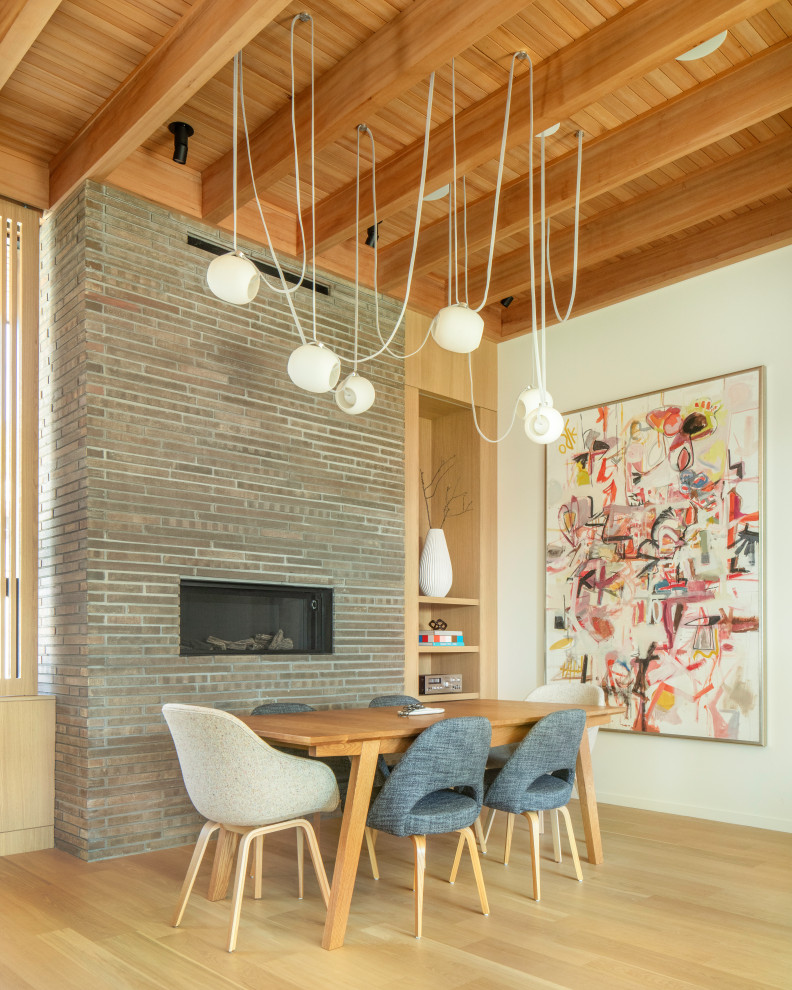 Aménagement d'une salle à manger ouverte sur le salon rétro en bois avec un mur blanc, parquet clair, une cheminée ribbon, un manteau de cheminée en brique et un plafond en bois.
