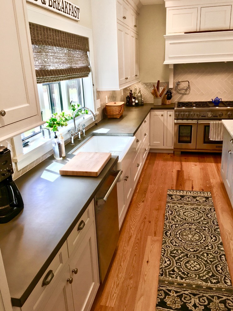 Transitional light wood floor and brown floor kitchen photo in New York with a farmhouse sink, white cabinets, concrete countertops, white backsplash, porcelain backsplash and stainless steel appliances