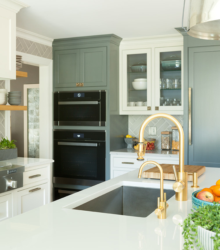 Design ideas for a mid-sized transitional u-shaped eat-in kitchen in New York with an undermount sink, glass-front cabinets, glass benchtops, grey splashback, ceramic splashback, with island, green cabinets, black appliances and white benchtop.