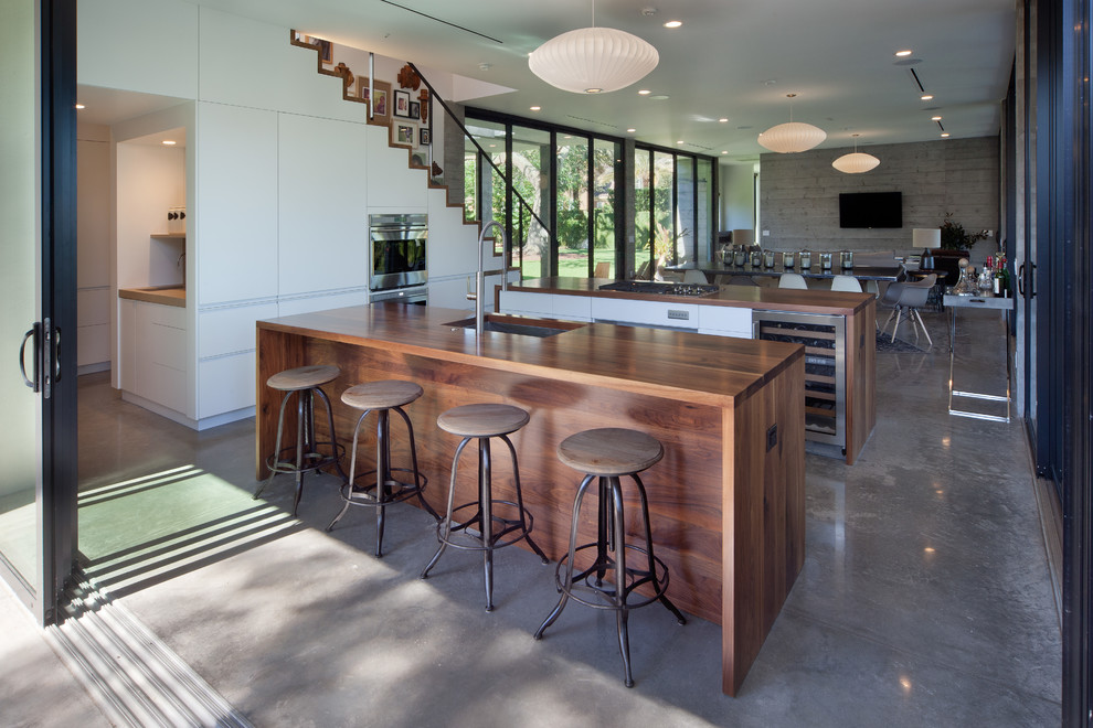 Inspiration for a large midcentury single-wall open plan kitchen in Orlando with an undermount sink, flat-panel cabinets, white cabinets, wood benchtops, stainless steel appliances, concrete floors, multiple islands, grey floor and brown benchtop.