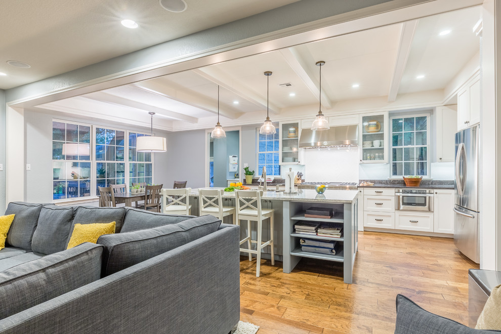 Example of a mid-sized transitional l-shaped medium tone wood floor eat-in kitchen design in Austin with an undermount sink, shaker cabinets, white cabinets, granite countertops, white backsplash, ceramic backsplash, stainless steel appliances and an island