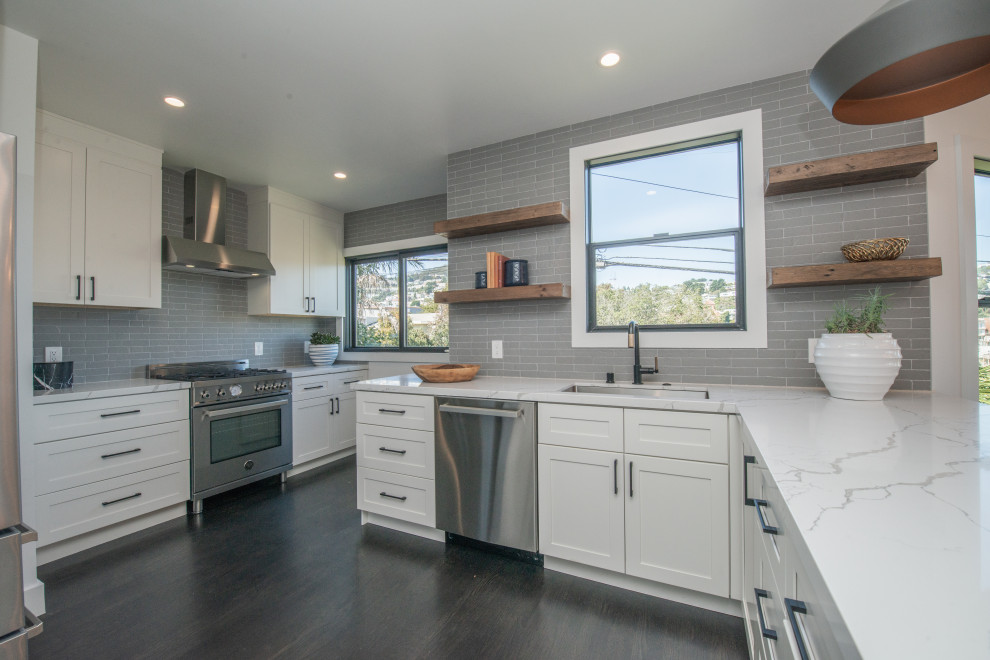 Inspiration for a large coastal l-shaped dark wood floor and brown floor open concept kitchen remodel in Los Angeles with an undermount sink, shaker cabinets, white cabinets, quartz countertops, gray backsplash, subway tile backsplash, stainless steel appliances, a peninsula and white countertops