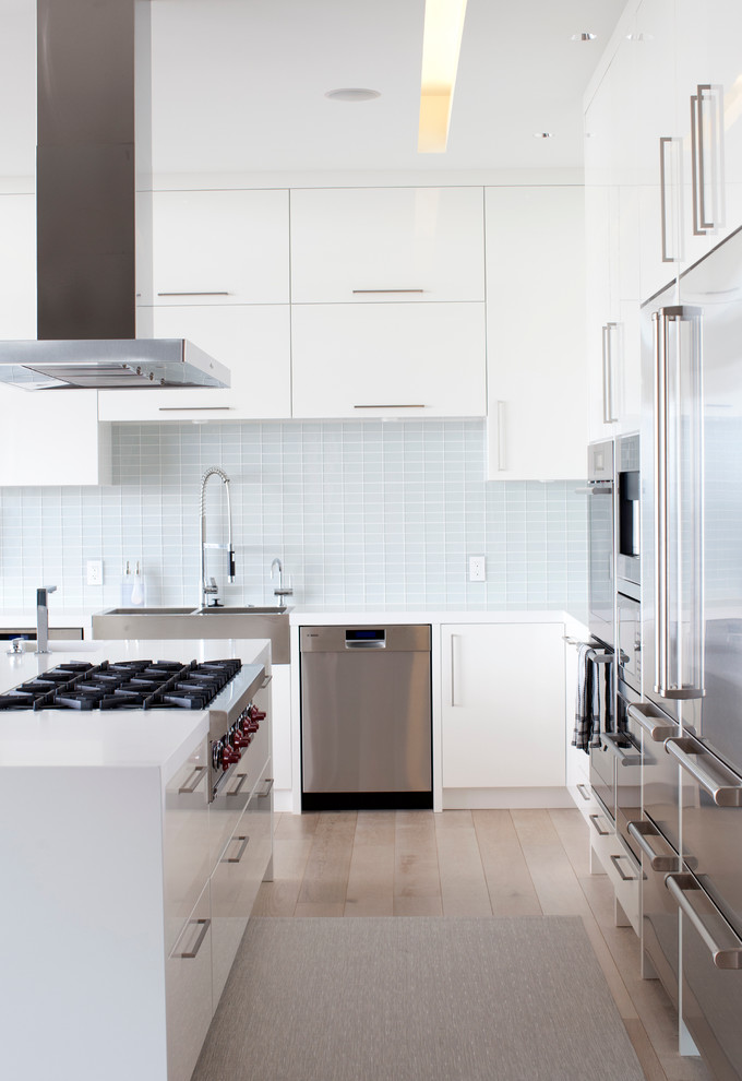 Design ideas for a modern l-shaped eat-in kitchen in Vancouver with a farmhouse sink, flat-panel cabinets, white cabinets, white splashback, glass tile splashback, stainless steel appliances and quartz benchtops.