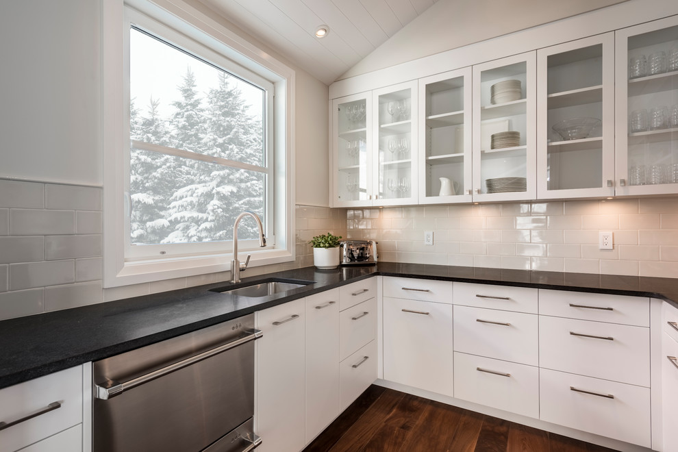 Inspiration for a mid-sized transitional l-shaped medium tone wood floor kitchen pantry remodel with a drop-in sink, flat-panel cabinets, white cabinets, white backsplash, ceramic backsplash, stainless steel appliances, an island, gray countertops and granite countertops