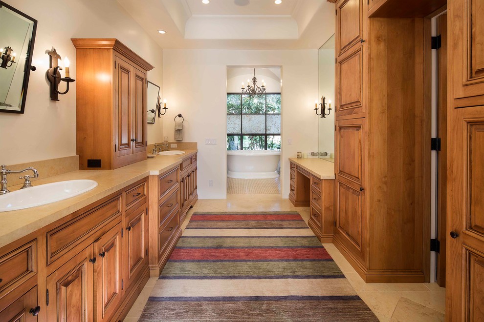 Inspiration for a large mediterranean master bathroom in Santa Barbara with raised-panel cabinets, medium wood cabinets, a freestanding tub, white walls, travertine floors and a drop-in sink.