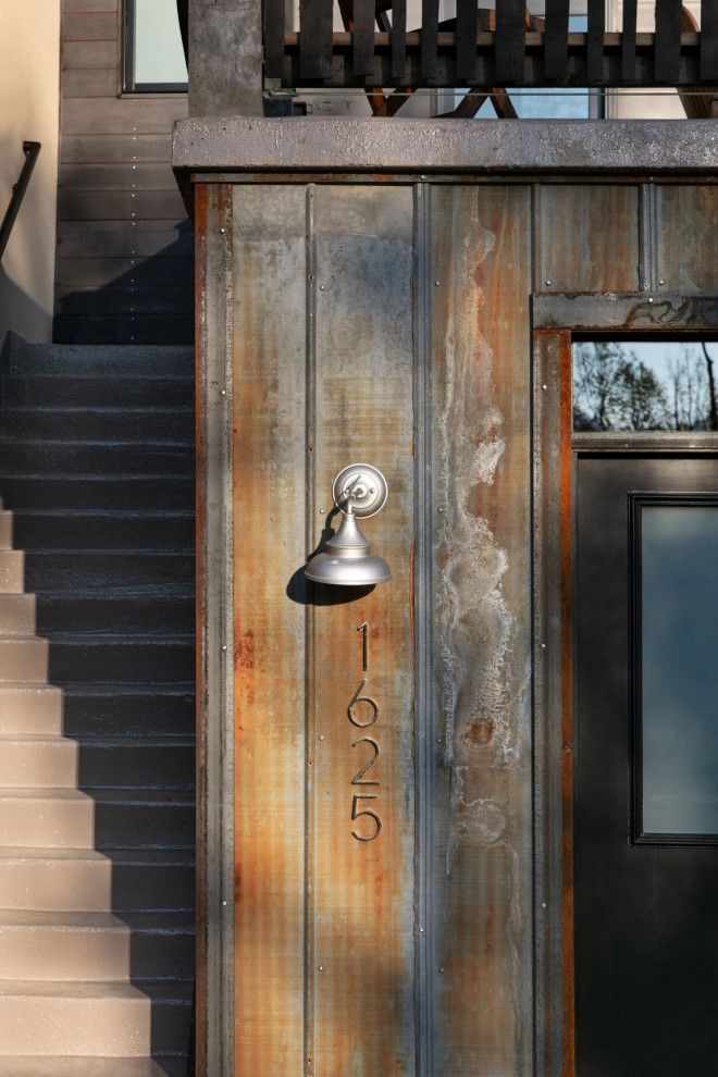 Foto della facciata di una casa piccola grigia contemporanea a piani sfalsati con rivestimento in cemento, copertura in metallo o lamiera, tetto nero e pannelli e listelle di legno