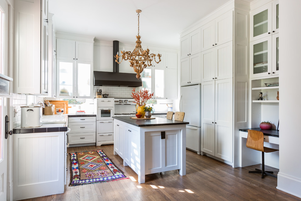 This is an example of a mid-sized transitional u-shaped eat-in kitchen in Houston with an undermount sink, shaker cabinets, white cabinets, white splashback, subway tile splashback, white appliances, dark hardwood floors, with island, tile benchtops and brown floor.