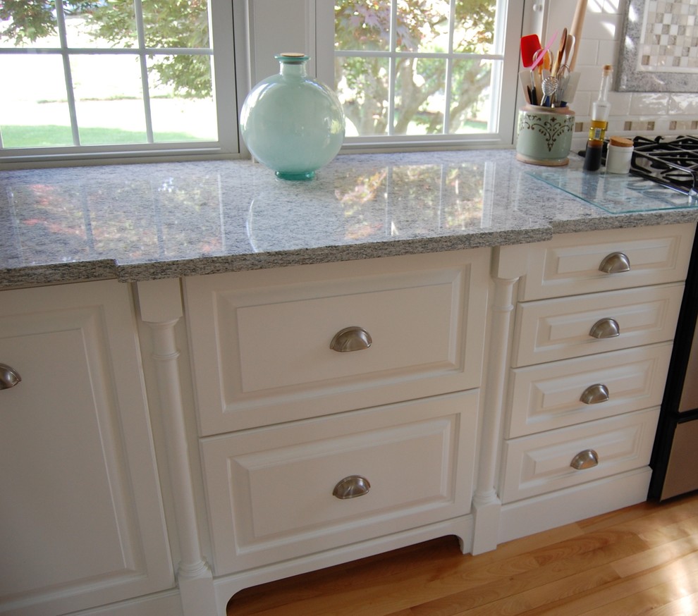 Inspiration for a mid-sized beach style u-shaped eat-in kitchen in Boston with an undermount sink, raised-panel cabinets, white cabinets, granite benchtops, white splashback, subway tile splashback, stainless steel appliances, light hardwood floors and a peninsula.