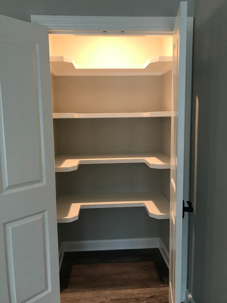 This is an example of a large transitional gender-neutral walk-in wardrobe in Houston with raised-panel cabinets, white cabinets, laminate floors and brown floor.