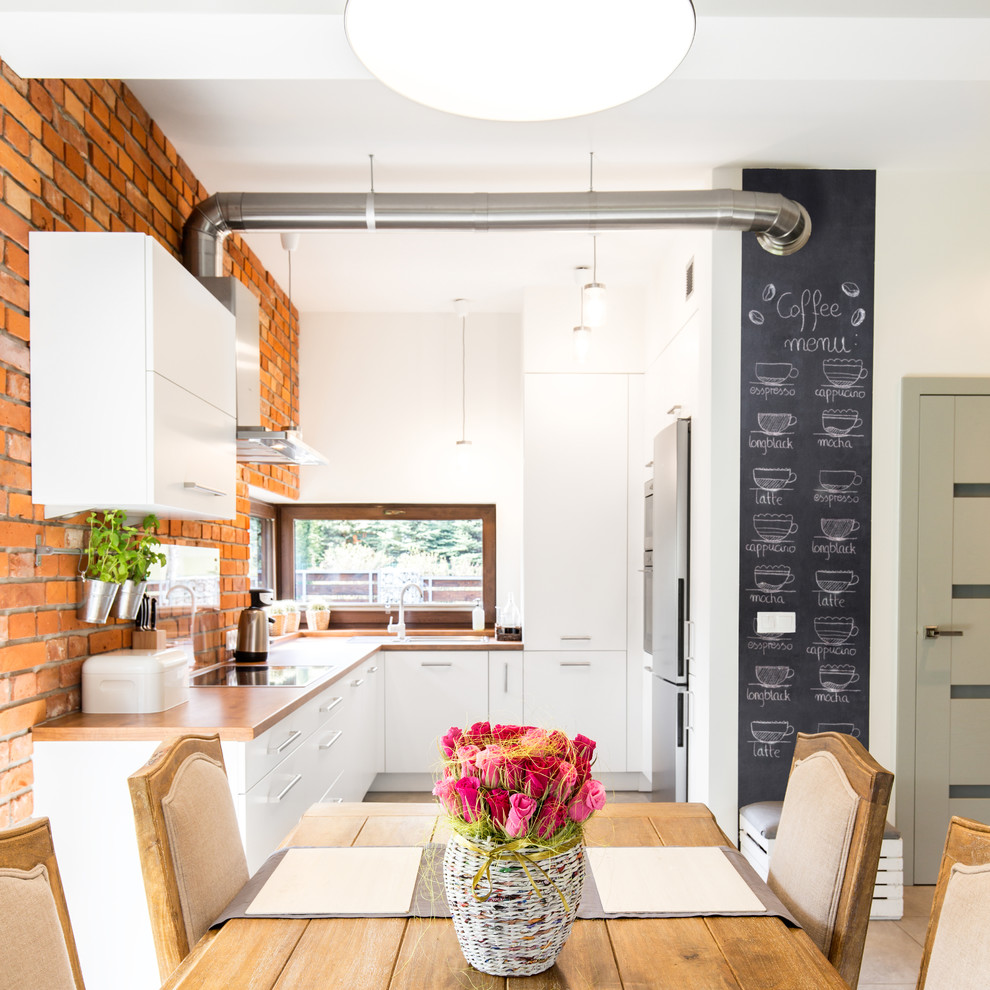 This is an example of a mid-sized scandinavian u-shaped eat-in kitchen in Los Angeles with a single-bowl sink, flat-panel cabinets, white cabinets, wood benchtops, red splashback, brick splashback, stainless steel appliances, porcelain floors, no island and beige floor.
