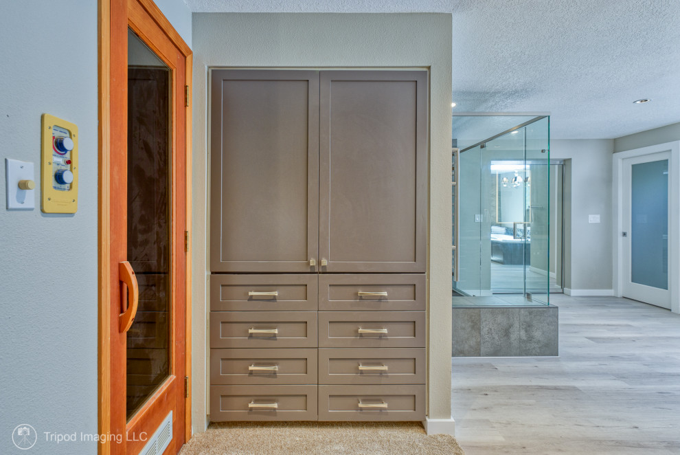 Photo of an expansive transitional master bathroom in Portland with shaker cabinets, brown cabinets, a drop-in tub, a corner shower, a two-piece toilet, gray tile, porcelain tile, grey walls, vinyl floors, an undermount sink, quartzite benchtops, grey floor, a hinged shower door, grey benchtops, a double vanity and a built-in vanity.