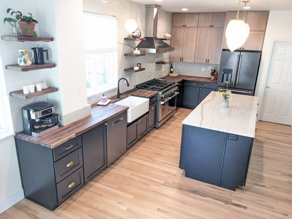 Example of a large transitional l-shaped kitchen design in Denver with a farmhouse sink, shaker cabinets, black cabinets, quartzite countertops, granite backsplash, black appliances, an island and white countertops
