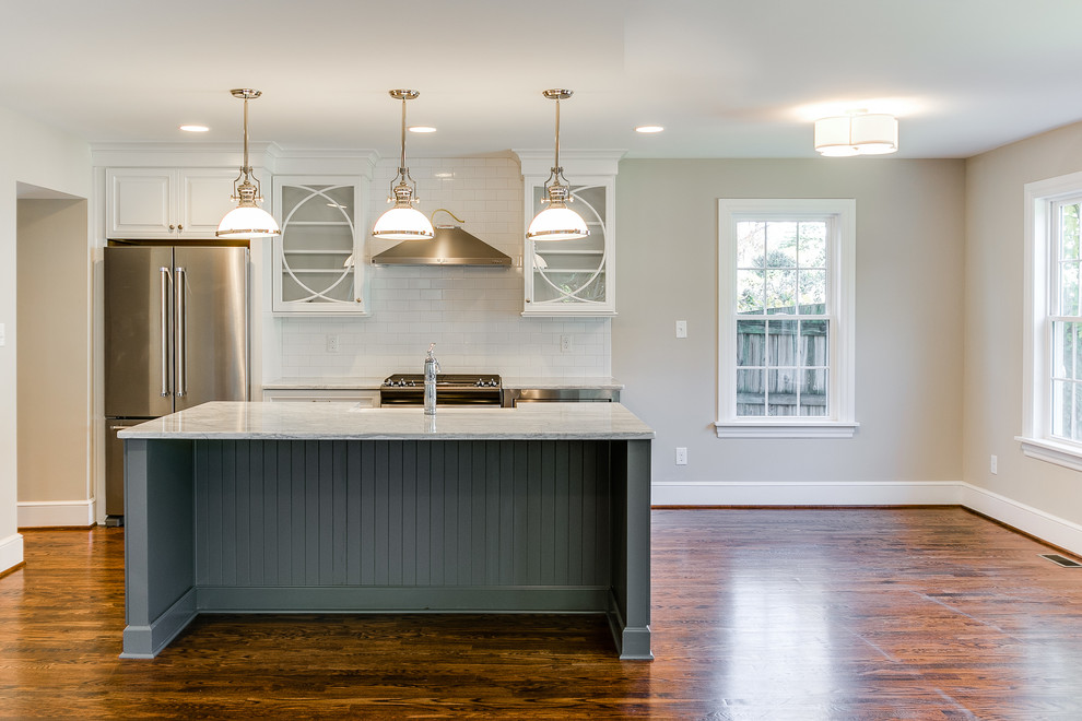 Single-wall medium tone wood floor eat-in kitchen photo in Richmond with a farmhouse sink, glass-front cabinets, white cabinets, marble countertops, white backsplash, subway tile backsplash, stainless steel appliances and an island
