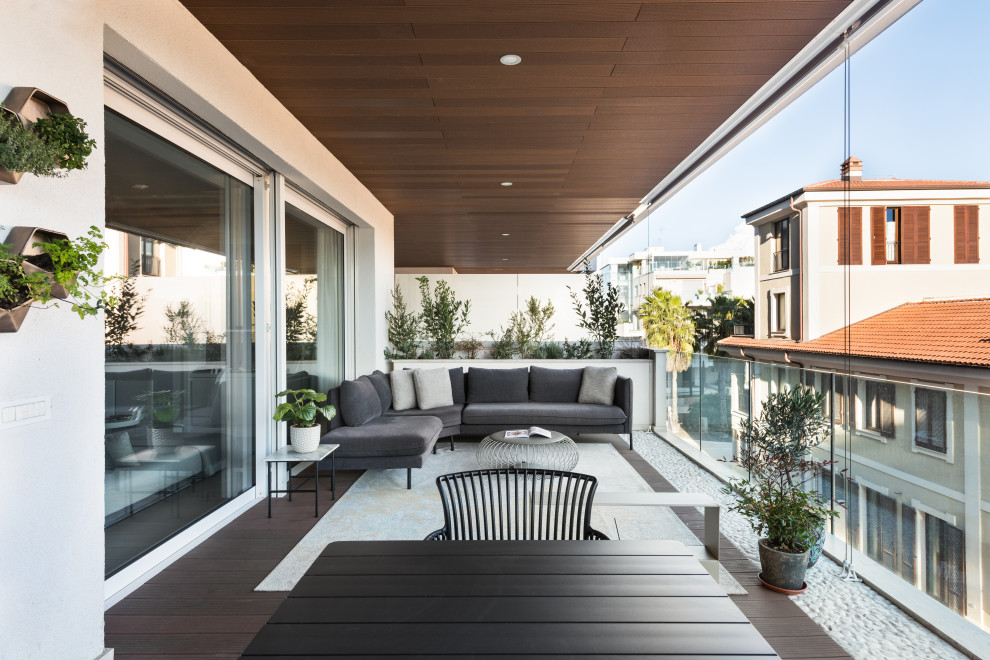 Photo of a large modern courtyard and first floor deck in Rome with with fireplace, a roof extension and glass railing.