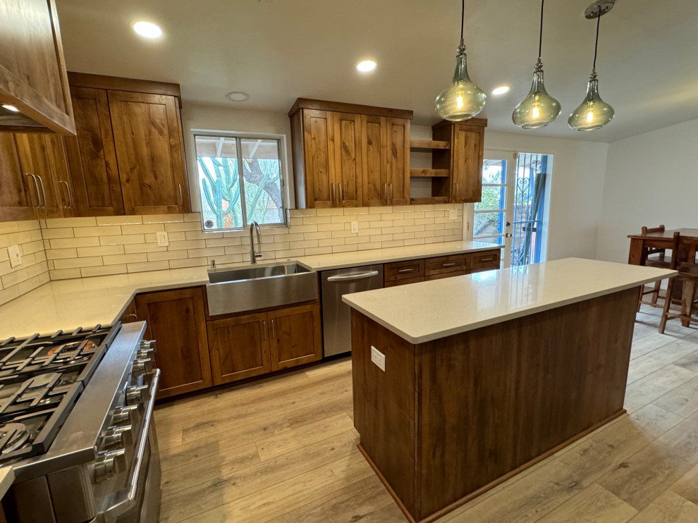 Example of a mid-sized transitional u-shaped laminate floor and beige floor eat-in kitchen design in Phoenix with a farmhouse sink, shaker cabinets, medium tone wood cabinets, quartz countertops, white backsplash, porcelain backsplash, stainless steel appliances, an island and beige countertops