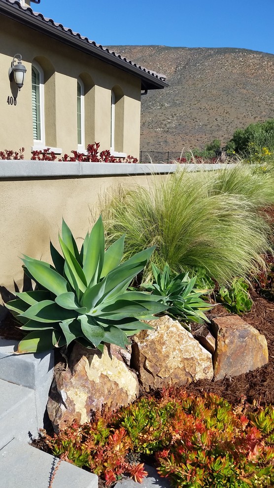 This is an example of a large mediterranean front yard full sun xeriscape in San Diego with concrete pavers.