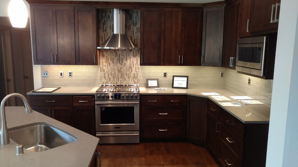 Example of a large transitional l-shaped medium tone wood floor eat-in kitchen design in Seattle with a single-bowl sink, recessed-panel cabinets, dark wood cabinets, quartz countertops, gray backsplash, glass tile backsplash, stainless steel appliances and an island