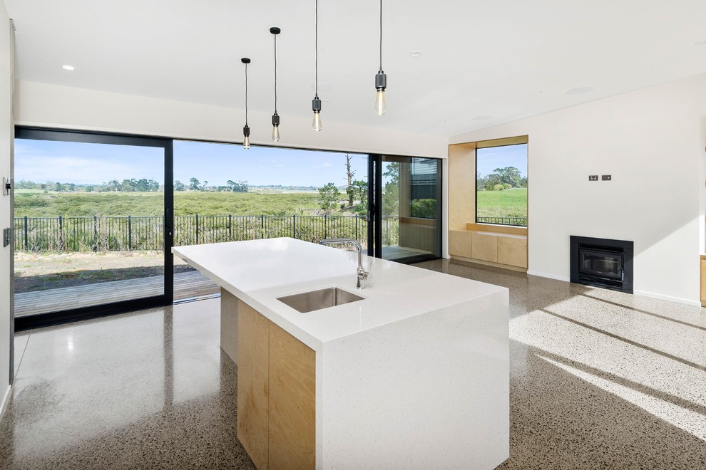 This is an example of a large contemporary l-shaped eat-in kitchen in Auckland with a drop-in sink, raised-panel cabinets, white cabinets, grey splashback, glass sheet splashback, concrete floors, with island, beige floor and white benchtop.