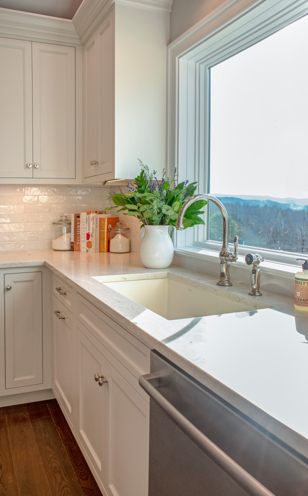 Transitional medium tone wood floor and brown floor eat-in kitchen photo with an undermount sink, shaker cabinets, white cabinets, quartz countertops, white backsplash, ceramic backsplash, stainless steel appliances and white countertops