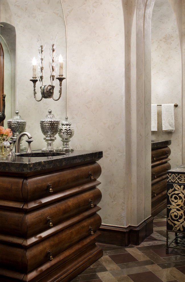 This is an example of a mediterranean powder room in Austin with dark wood cabinets and beige tile.