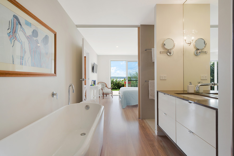 Inspiration for a mid-sized beach style master bathroom in Other with white cabinets, a freestanding tub, an open shower, mirror tile, white walls, light hardwood floors, a drop-in sink, white floor and an open shower.
