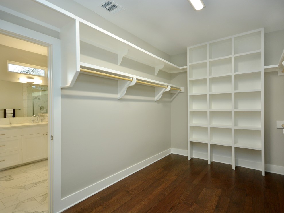 This is an example of a large arts and crafts gender-neutral walk-in wardrobe in Austin with white cabinets and dark hardwood floors.