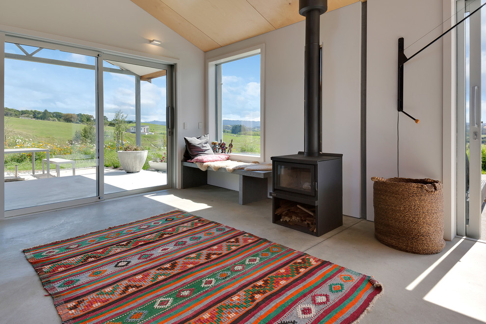 This is an example of a mid-sized contemporary open concept living room in Auckland with white walls, concrete floors, a wood stove, a wall-mounted tv and grey floor.