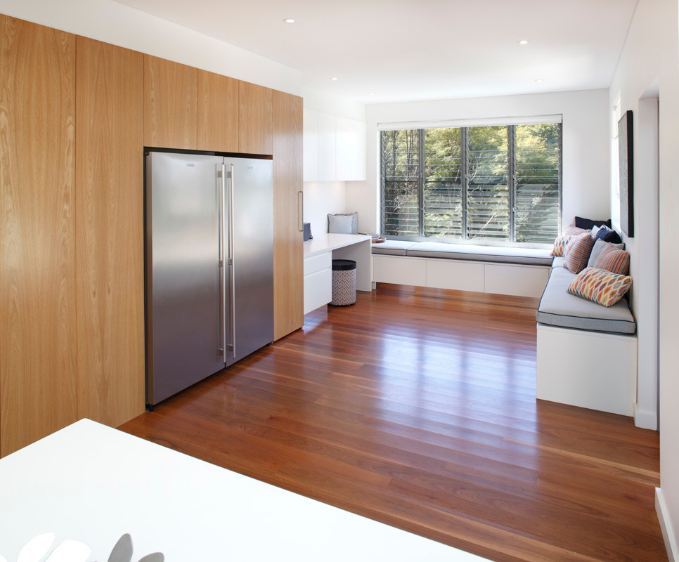 This is an example of a large contemporary galley open plan kitchen in Sydney with an undermount sink, flat-panel cabinets, white cabinets, quartzite benchtops, white splashback, glass sheet splashback, stainless steel appliances, medium hardwood floors and a peninsula.