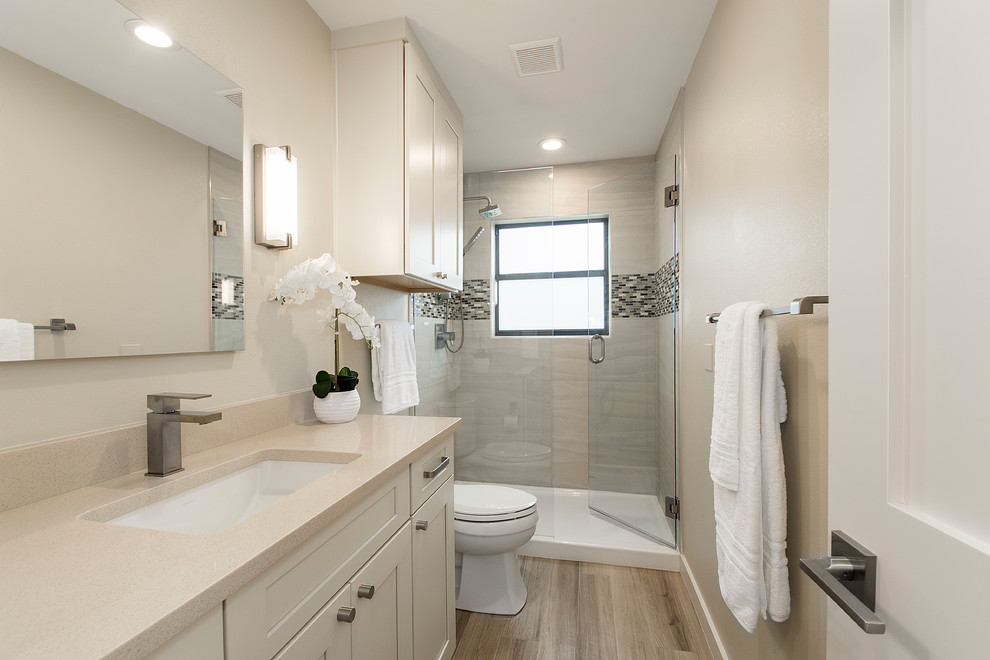 Large transitional 3/4 bathroom in Dallas with beige walls, light hardwood floors, beige floor, flat-panel cabinets, white cabinets, a corner shower, a one-piece toilet, beige tile, porcelain tile, an undermount sink, engineered quartz benchtops and a hinged shower door.