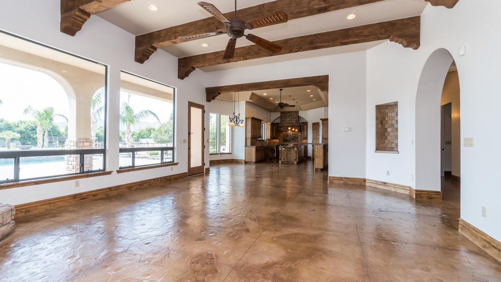 Photo of an expansive mediterranean open concept family room in Phoenix with white walls, concrete floors, a corner fireplace, a stone fireplace surround, no tv and brown floor.