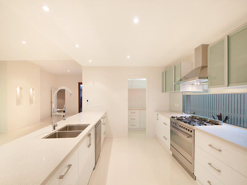 Mid-sized modern galley kitchen pantry in Melbourne with an undermount sink, flat-panel cabinets, white cabinets, solid surface benchtops, white splashback, glass sheet splashback, stainless steel appliances, marble floors and with island.