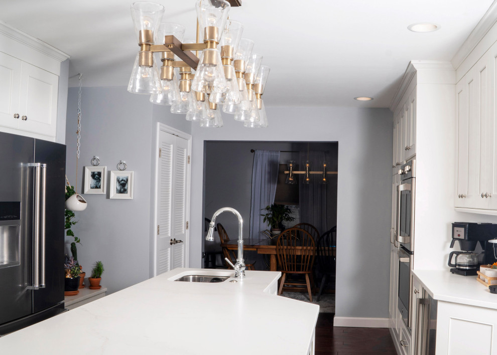 Mid-sized transitional l-shaped medium tone wood floor and brown floor eat-in kitchen photo in St Louis with a farmhouse sink, recessed-panel cabinets, white cabinets, quartz countertops, blue backsplash, ceramic backsplash, stainless steel appliances, an island and white countertops