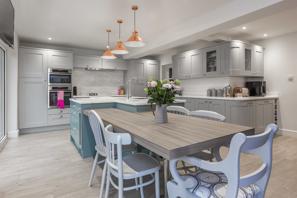 Photo of a large transitional l-shaped kitchen in Dorset with grey cabinets, stainless steel appliances, light hardwood floors, an undermount sink, shaker cabinets, grey splashback and multiple islands.