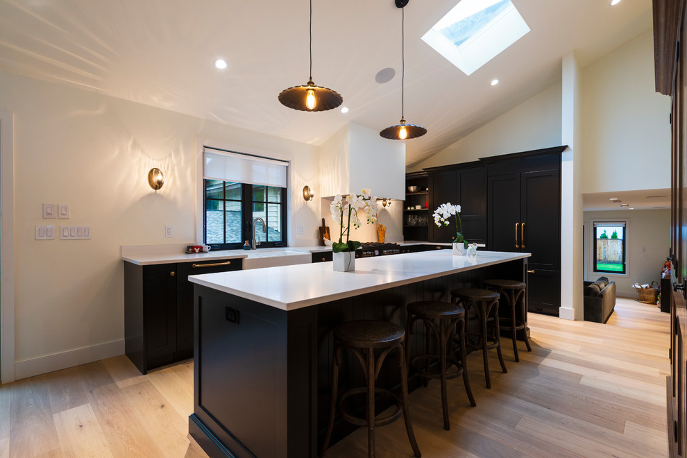 Inspiration for a mid-sized rustic l-shaped light wood floor and beige floor open concept kitchen remodel in Vancouver with a farmhouse sink, shaker cabinets, black cabinets, quartz countertops, paneled appliances, an island and white countertops