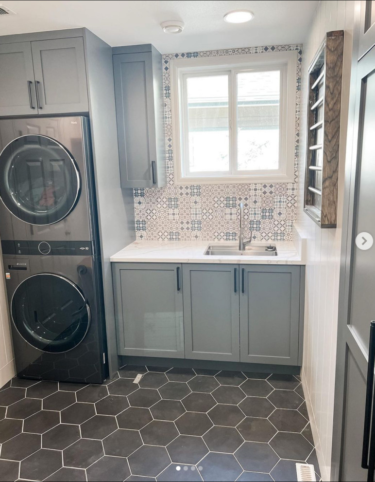 Small country utility room in Seattle with an utility sink, recessed-panel cabinets, grey cabinets, white splashback, porcelain splashback, white walls, ceramic floors, a stacked washer and dryer, grey floor, white benchtop and planked wall panelling.