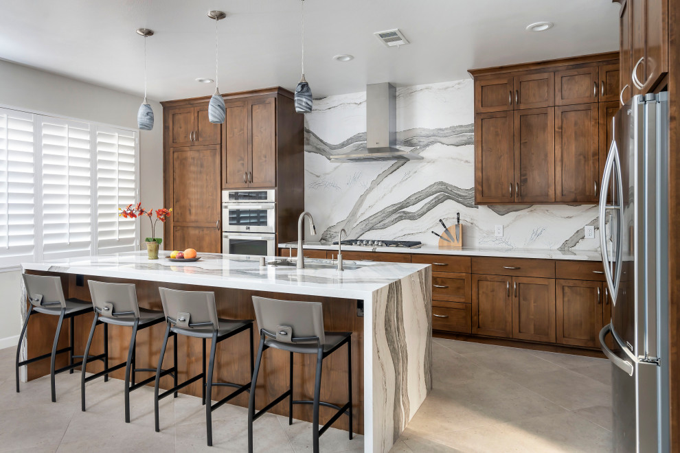 This is an example of a large transitional l-shaped open plan kitchen in Los Angeles with an undermount sink, shaker cabinets, medium wood cabinets, quartz benchtops, white splashback, engineered quartz splashback, stainless steel appliances, ceramic floors, with island, white benchtop and grey floor.