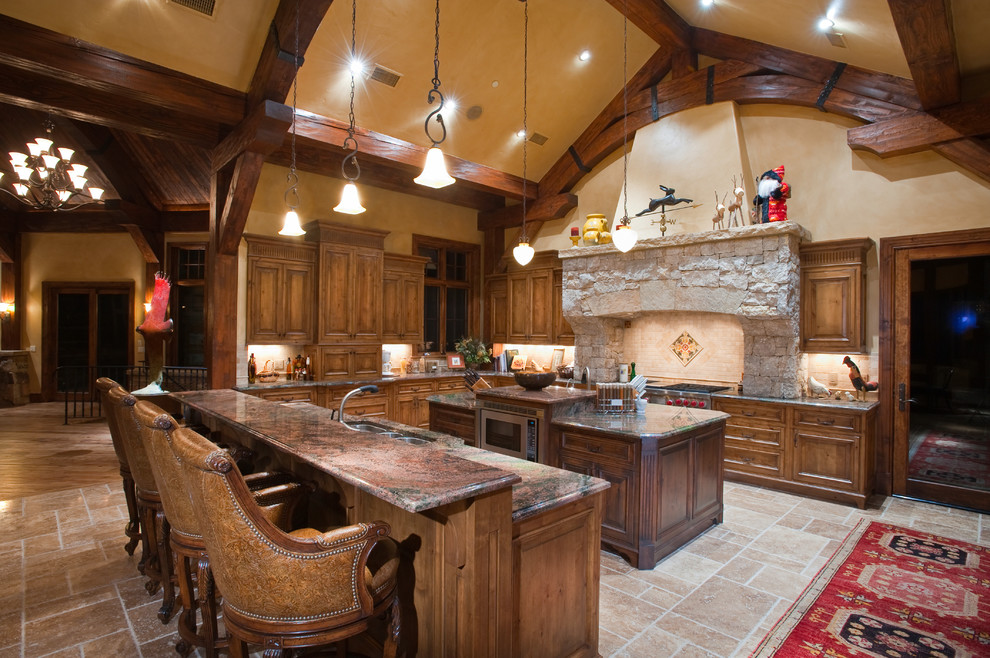 Eat-in kitchen - large rustic l-shaped limestone floor, beige floor and vaulted ceiling eat-in kitchen idea in Denver with an undermount sink, raised-panel cabinets, medium tone wood cabinets, granite countertops, beige backsplash, stone tile backsplash, stainless steel appliances and two islands