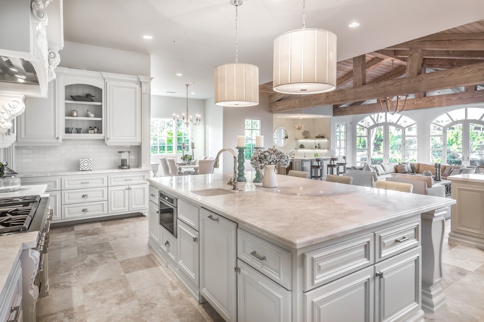 Photo of a large traditional l-shaped open plan kitchen in San Diego with raised-panel cabinets, white cabinets, quartzite benchtops, white splashback, subway tile splashback, travertine floors, with island and beige floor.